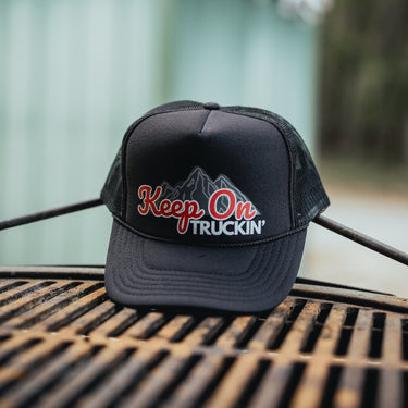 Black trucker hat with 'Keep On Truckin'' text and mountain graphic product shot