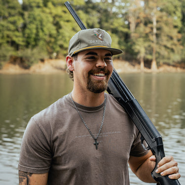 Man holding a rifle wearing Smoke & Steel green hat with rope with duck design