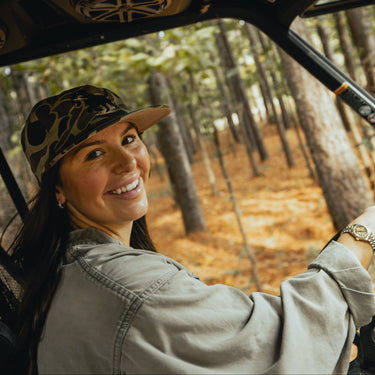 Old school duck camo cap with embroidered dog design on model in the woods
